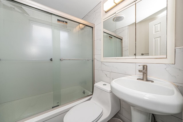 bathroom featuring tile walls, decorative backsplash, toilet, combined bath / shower with glass door, and a sink