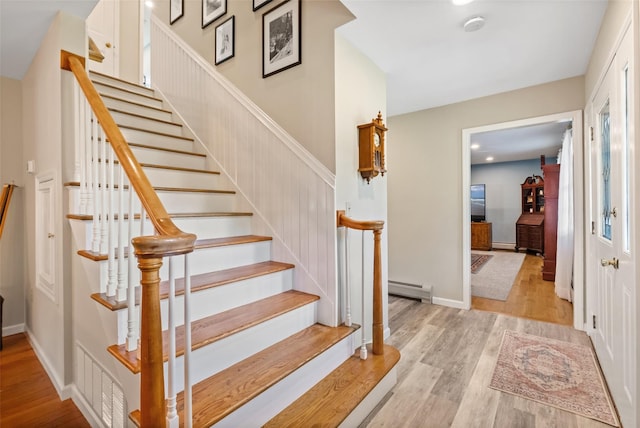 stairway with a baseboard radiator, baseboards, and wood finished floors