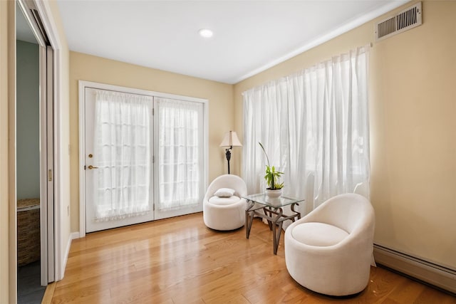 living area with baseboard heating, wood finished floors, and visible vents