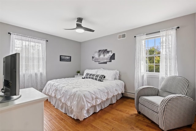 bedroom with a baseboard heating unit, light wood-style flooring, visible vents, and a ceiling fan