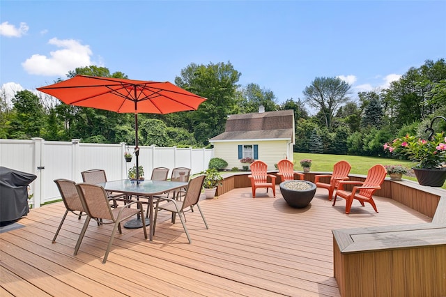 wooden deck featuring a fire pit, an outbuilding, a grill, fence, and outdoor dining space