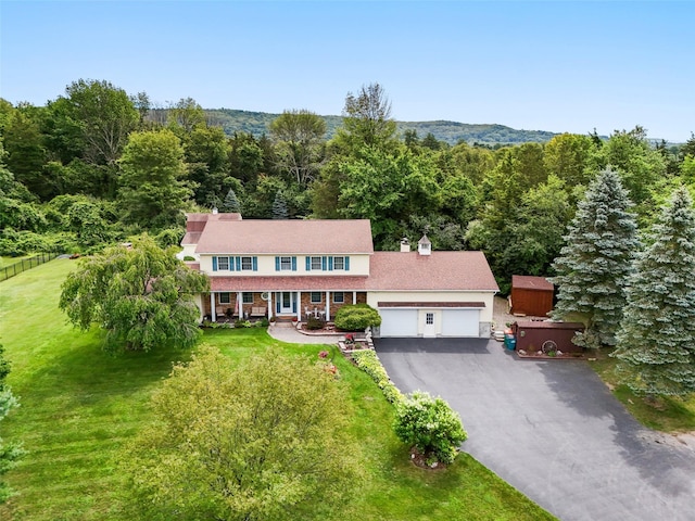 view of front facade featuring driveway, a garage, a front lawn, and a wooded view