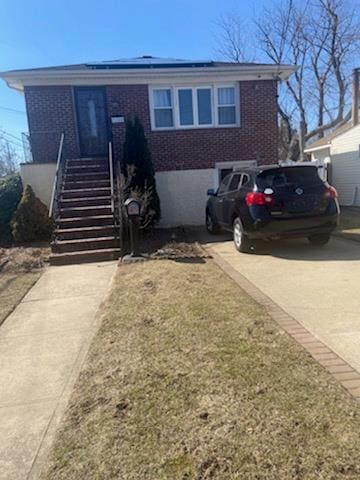 view of front of house featuring concrete driveway, brick siding, stairway, and roof mounted solar panels