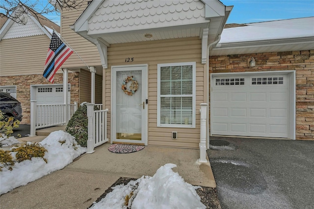 doorway to property with an attached garage, stone siding, and aphalt driveway