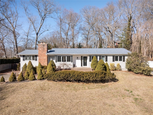 ranch-style house with a shingled roof, a chimney, and a front lawn