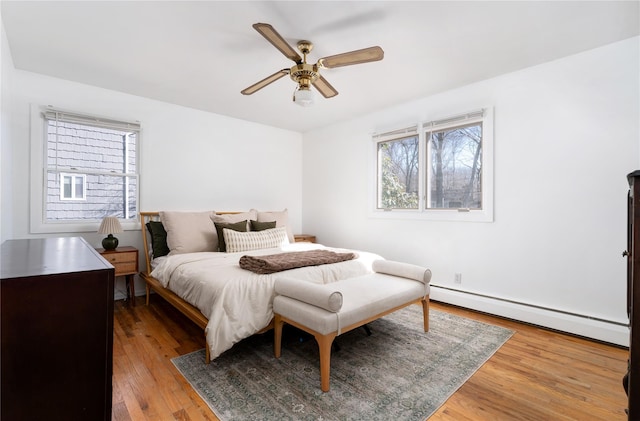 bedroom with light wood-type flooring, multiple windows, a baseboard radiator, and a ceiling fan