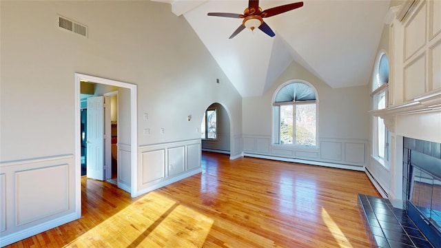 unfurnished living room with visible vents, a ceiling fan, a tiled fireplace, light wood-style flooring, and a baseboard heating unit