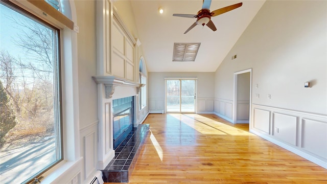 living room with visible vents, a decorative wall, light wood-style flooring, a tiled fireplace, and vaulted ceiling