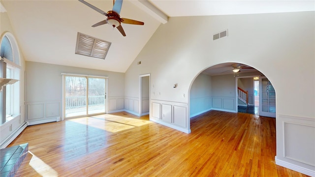 empty room with visible vents, arched walkways, stairway, light wood-type flooring, and beam ceiling