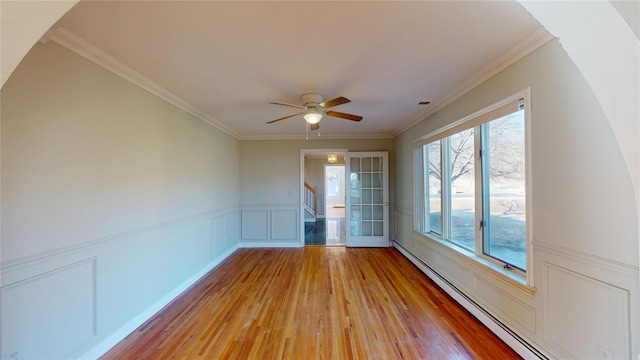 spare room featuring a wainscoted wall, a baseboard radiator, light wood-style flooring, ornamental molding, and ceiling fan