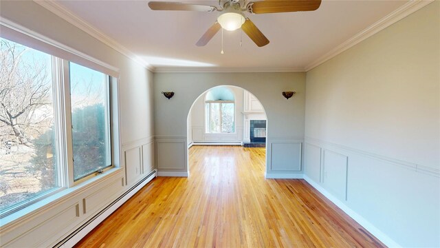 unfurnished room with a baseboard heating unit, a wainscoted wall, light wood-style floors, and ornamental molding