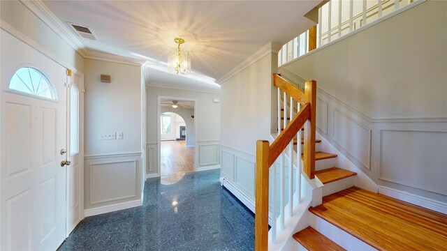 foyer featuring a decorative wall, a wainscoted wall, granite finish floor, stairs, and crown molding