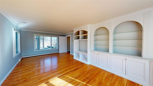 empty room featuring light wood finished floors, baseboards, crown molding, built in shelves, and a baseboard heating unit