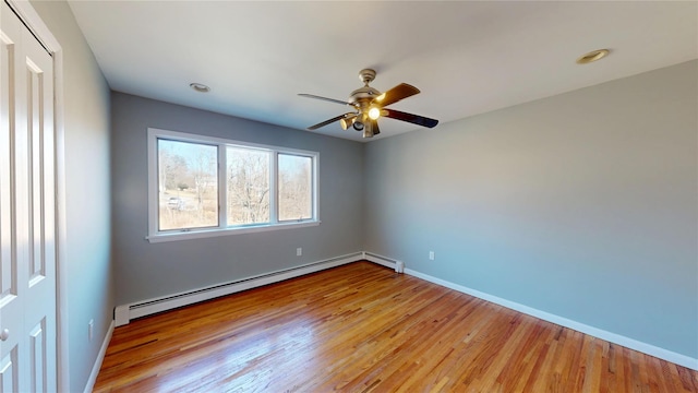 spare room featuring a baseboard heating unit, wood finished floors, and baseboards