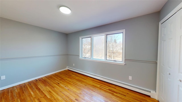 unfurnished bedroom with light wood-style floors, a baseboard radiator, a closet, and baseboards