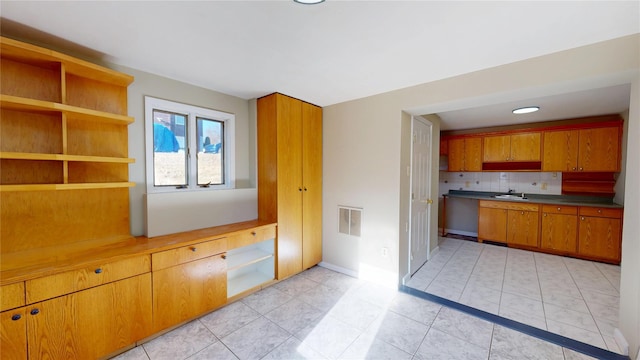 kitchen with light tile patterned floors, visible vents, backsplash, brown cabinetry, and a sink