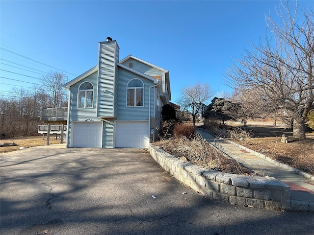 view of side of home with aphalt driveway, a chimney, and an attached garage