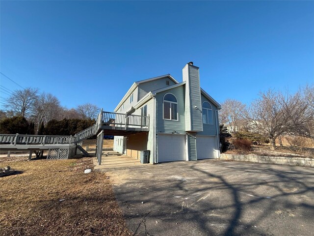 view of property exterior featuring a chimney, stairway, an attached garage, driveway, and a wooden deck