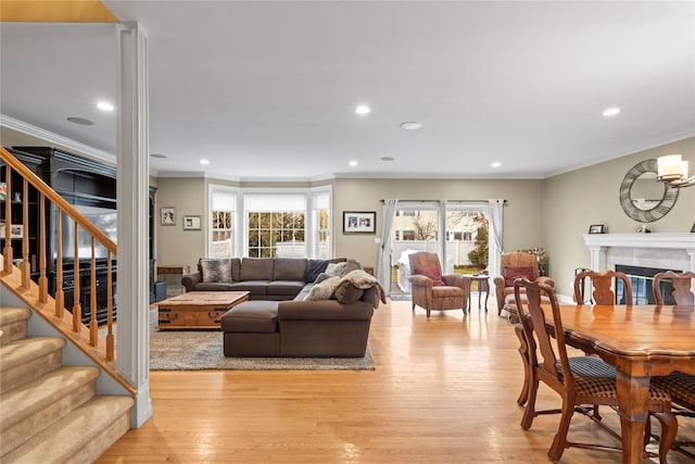 living area featuring stairway, a tile fireplace, light wood-style flooring, and crown molding