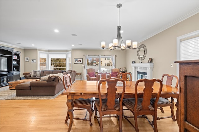 dining area with ornamental molding, a fireplace, light wood-style floors, and a notable chandelier