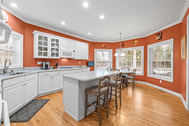 kitchen with white appliances, light wood-style flooring, ornamental molding, a breakfast bar, and a sink