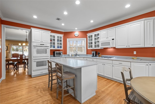 kitchen with glass insert cabinets, white appliances, a sink, and a breakfast bar area