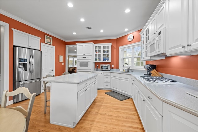 kitchen featuring white appliances, white cabinets, a kitchen breakfast bar, a center island, and light wood-type flooring