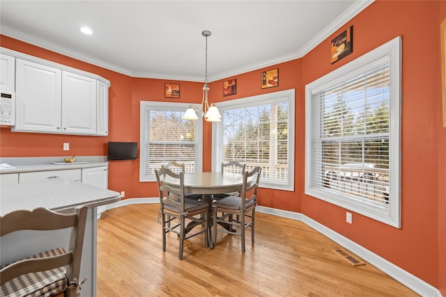 dining room with light wood-type flooring, a wealth of natural light, visible vents, and crown molding