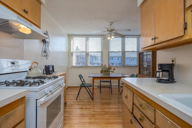 kitchen featuring a healthy amount of sunlight, under cabinet range hood, white range with gas stovetop, and light countertops