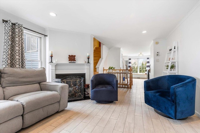 living room featuring a glass covered fireplace, recessed lighting, light wood-style floors, and ornamental molding