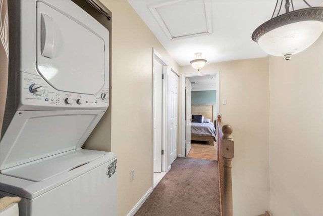 laundry area with carpet, stacked washer / dryer, baseboards, attic access, and laundry area