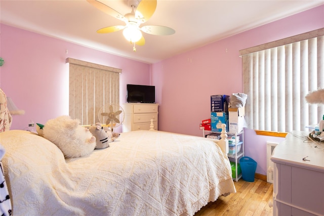 bedroom featuring radiator heating unit, wood finished floors, a ceiling fan, and baseboards