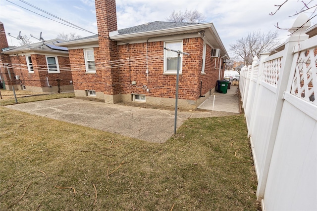 back of house featuring a patio, a fenced backyard, a chimney, a yard, and brick siding