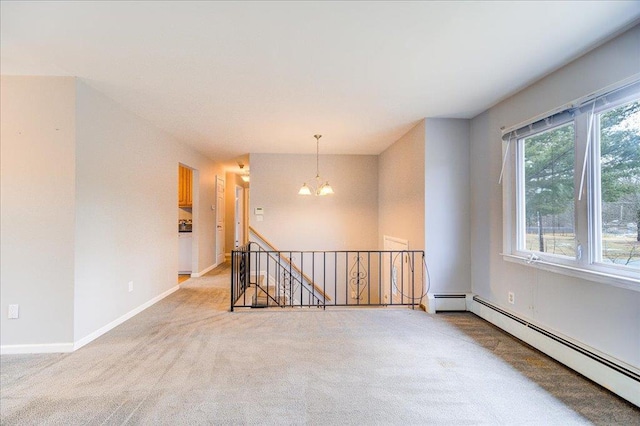 spare room featuring a chandelier, light carpet, a baseboard heating unit, and baseboards