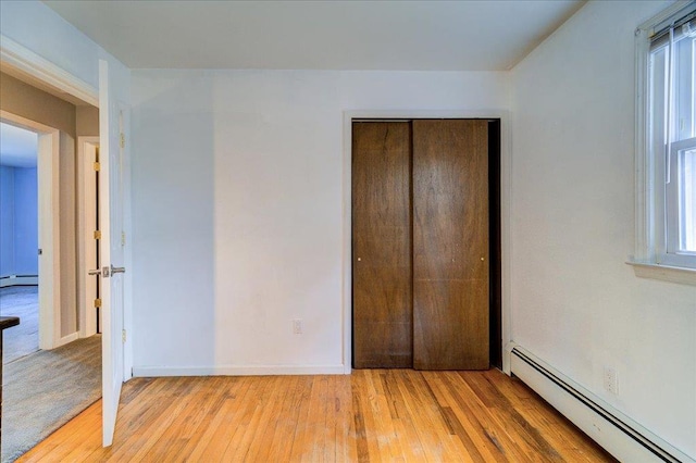 unfurnished bedroom with a baseboard heating unit, multiple windows, light wood-type flooring, and a closet