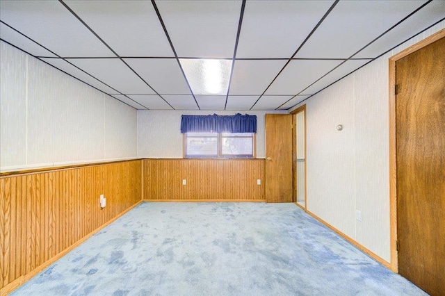 basement featuring a drop ceiling, carpet, and wood walls