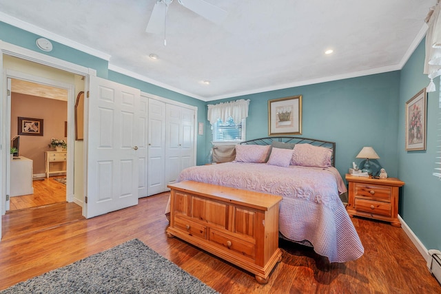 bedroom with baseboards, ornamental molding, wood finished floors, baseboard heating, and a closet