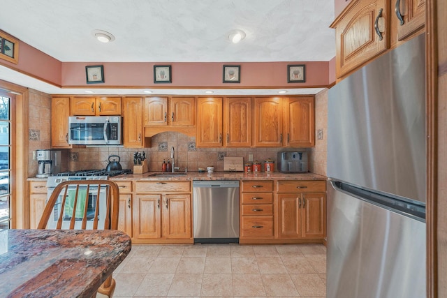 kitchen featuring appliances with stainless steel finishes, a sink, light stone countertops, and tasteful backsplash