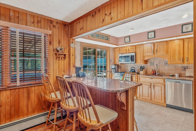 kitchen featuring stainless steel appliances, wood walls, a sink, baseboard heating, and backsplash