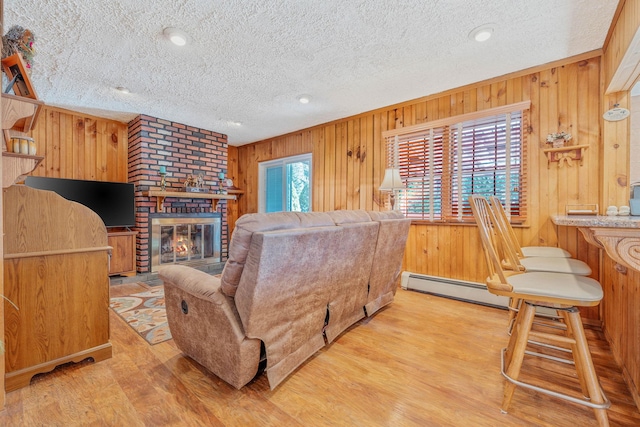 living room featuring light wood finished floors, baseboard heating, a fireplace, and wood walls