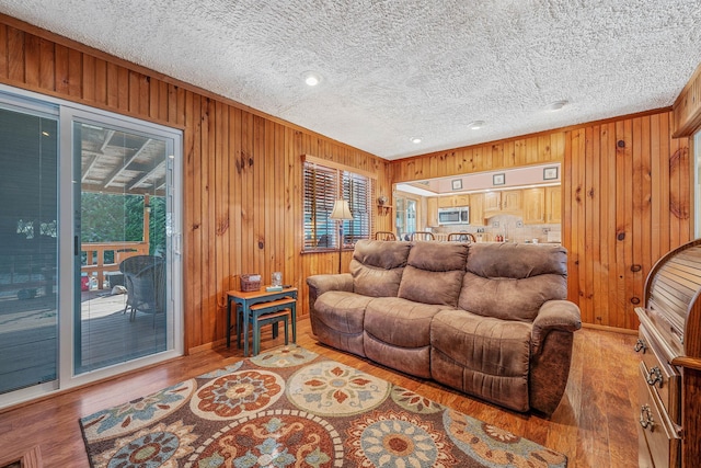 living room with a textured ceiling, wood walls, wood finished floors, baseboards, and crown molding