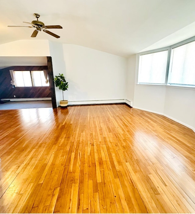 unfurnished living room featuring light wood-style floors, a baseboard heating unit, vaulted ceiling, and a wealth of natural light