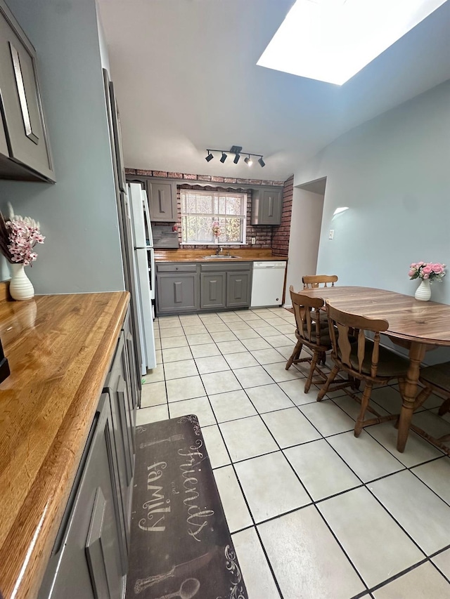 kitchen with light tile patterned floors, white appliances, a sink, wood counters, and gray cabinets