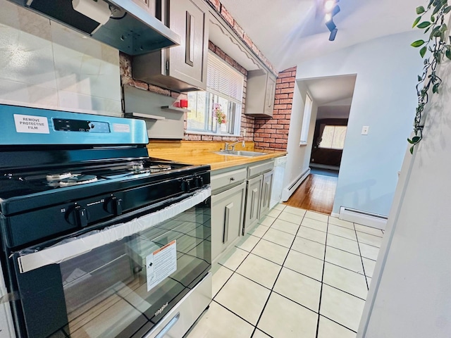 kitchen with a baseboard heating unit, light tile patterned flooring, stainless steel range with gas stovetop, a sink, and exhaust hood