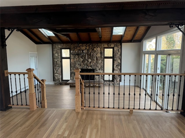 interior space with lofted ceiling with skylight, wood finished floors, a stone fireplace, wooden ceiling, and baseboards