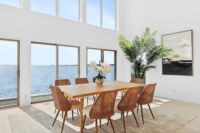 dining area with light wood finished floors, a towering ceiling, and a water view