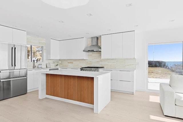 kitchen with high quality fridge, light countertops, wall chimney exhaust hood, range, and modern cabinets