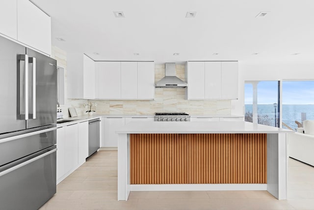 kitchen featuring tasteful backsplash, stainless steel appliances, light countertops, and wall chimney range hood