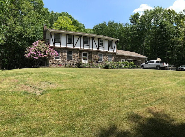 tudor-style house with stone siding, a chimney, a front yard, and stucco siding