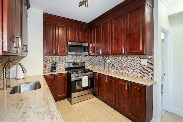 kitchen featuring appliances with stainless steel finishes, reddish brown cabinets, a sink, and light stone counters